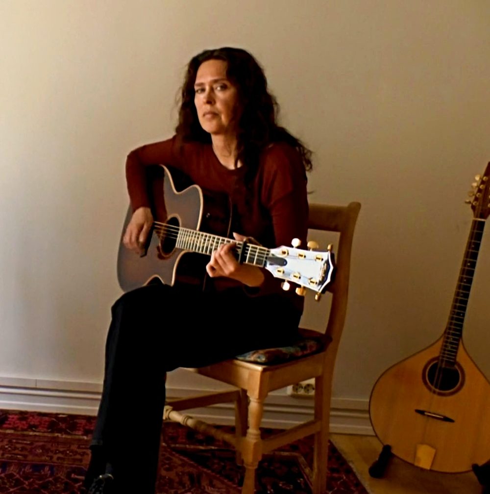 Viil sitting on a chair playing the guitar.